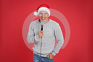 Happy man in Santa Claus hat singing with microphone on red background. Christmas music