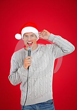 Happy man in Santa Claus hat singing with microphone on red background. Christmas music