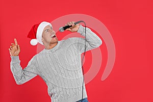 Happy man in Santa Claus hat singing with microphone on red background, space for text. Christmas music