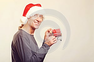 Happy man in Santa hat holding small shopping cart, copy space. Christmas sales and shopping concept. Handsome man shopper with