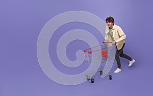 Happy man shopper holding shopping cart rushing next shop store  over purple background