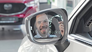 Happy man showing car keys to the camera through side mirror of his car