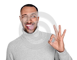 Happy young man showing his tongue and OK gesture on white background