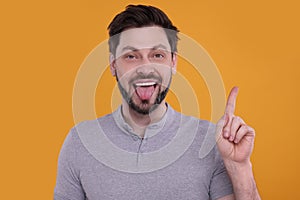Happy man showing his tongue and pointing on orange background