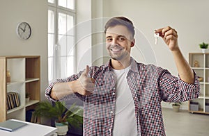 Happy man showing keys to his new house or apartment , smiling and giving thumbs up