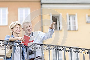 Happy man showing something to woman with guidebook in city