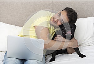 Happy man sits on the bed and hugs his lovely dog