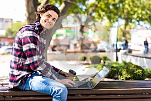 Happy man sitting on bench and using laptop in a park. Young man sitting on the park bench with laptop