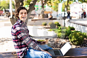 Happy man sitting on bench and using laptop in a park. Young man sitting on the park bench with laptop