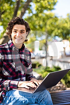 Happy man sitting on bench and using laptop in a park. Young man sitting on the park bench with laptop