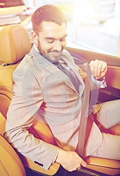 Happy man sitting in car at auto show or salon