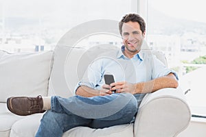 Happy man sitting on the couch using his smartphone