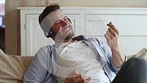 Happy man sitting on couch wearing headphones listening to music