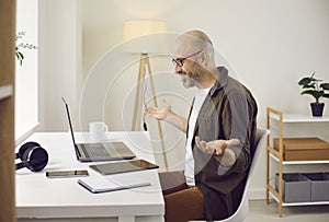 Happy man sitting in front of laptop in home office and having online work meeting