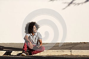 Happy man sitting on sidewalk outside with phone