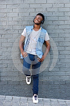 Happy man smiling with headphones leaning against wall