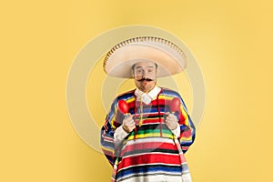 Happy man in sombrero and bright poncho isolated over yellow background