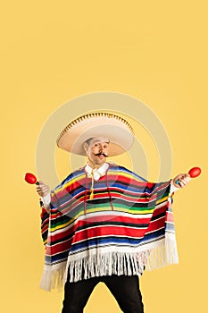 Happy man in sombrero and bright poncho isolated over yellow background