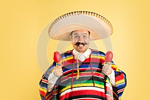 Happy man in sombrero and bright poncho isolated over yellow background