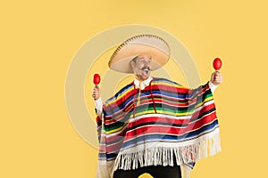 Happy man in sombrero and bright poncho isolated over yellow background