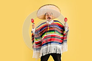 Happy man in sombrero and bright poncho isolated over yellow background