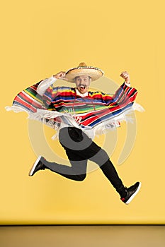 Happy man in sombrero and bright poncho isolated over yellow background