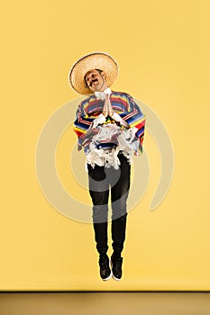 Happy man in sombrero and bright poncho isolated over yellow background