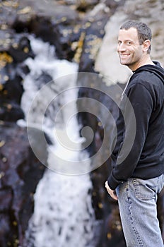 Happy man standing by a small rock waterfall.