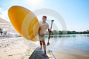 Happy man is standing with a SUP board on beach