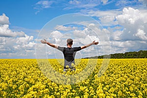 Happy man stands in a yellow field rejoicing raises his hands to the sky