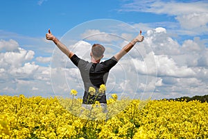 Happy man stands in a yellow field rejoicing raises his hands to the sky