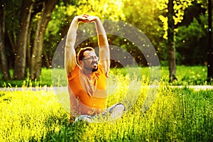A happy man is stretching himself on green grass with squint eye