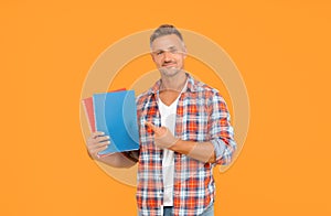 Happy man student pointing finger at copybooks yellow background, education