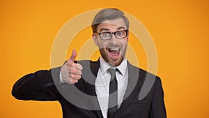 Happy man in suit showing thumbs up and winking at camera, good proposition