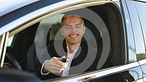 Happy man taking car key from dealer in auto show or salon. Car dealer giving key to new car owner. Businessman sitting