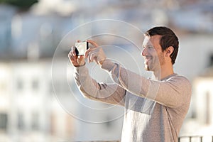 Happy man taking photos with mobile phone in a town