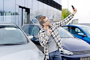 Happy man taking selfie through smart phone after purchasing new car. The man showing the purchased car via video link over the