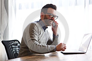 Happy man talking on cellphone in front of laptop computer