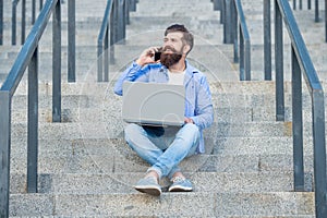 Happy man talking on mobile phone working on laptop. Smiling man making mobile call on stairs