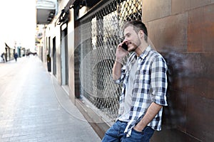 Happy man talks on phone leaning on a wall in the street