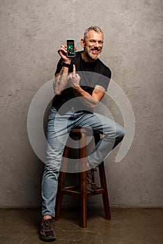 Happy man with tattoo pointing with finger at smartphone with charts and graphs