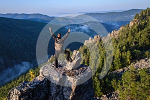 Happy man traveller standing with raised hands on mountain top and celebrating success.