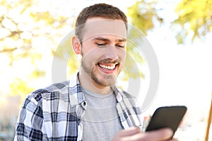 Happy man uses a smart phone walking in a park