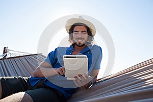 Happy man using digital tablet on hammock at beach