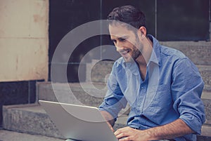Happy man using his laptop computer outdoors smiling