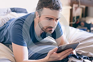 Happy man using his tablet lying in bed