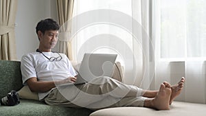 Happy man using laptop computer while relaxing on a comfortable couch at home.