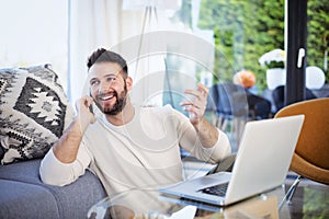 Happy man using mobile phone and laptop while sitting in the sitting room at home