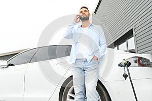 Happy man using smart phone and charging car at vehicle charging station