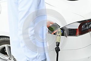 Happy man using smart phone and charging car at vehicle charging station